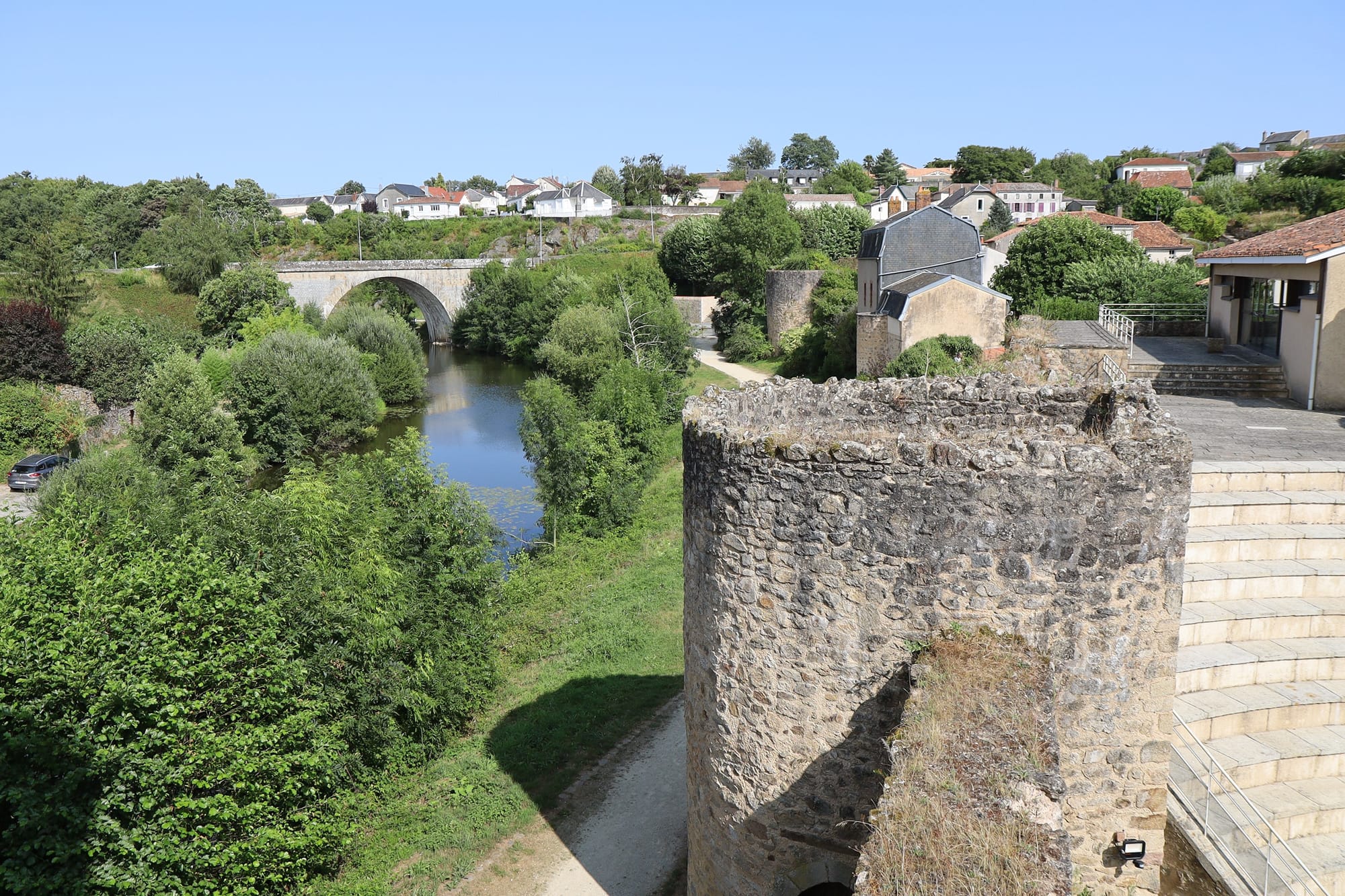 Vue des anciens remparts de Parthenay avec la rivière et son pont de pierre, entourés de verdure et de maisons pittoresques