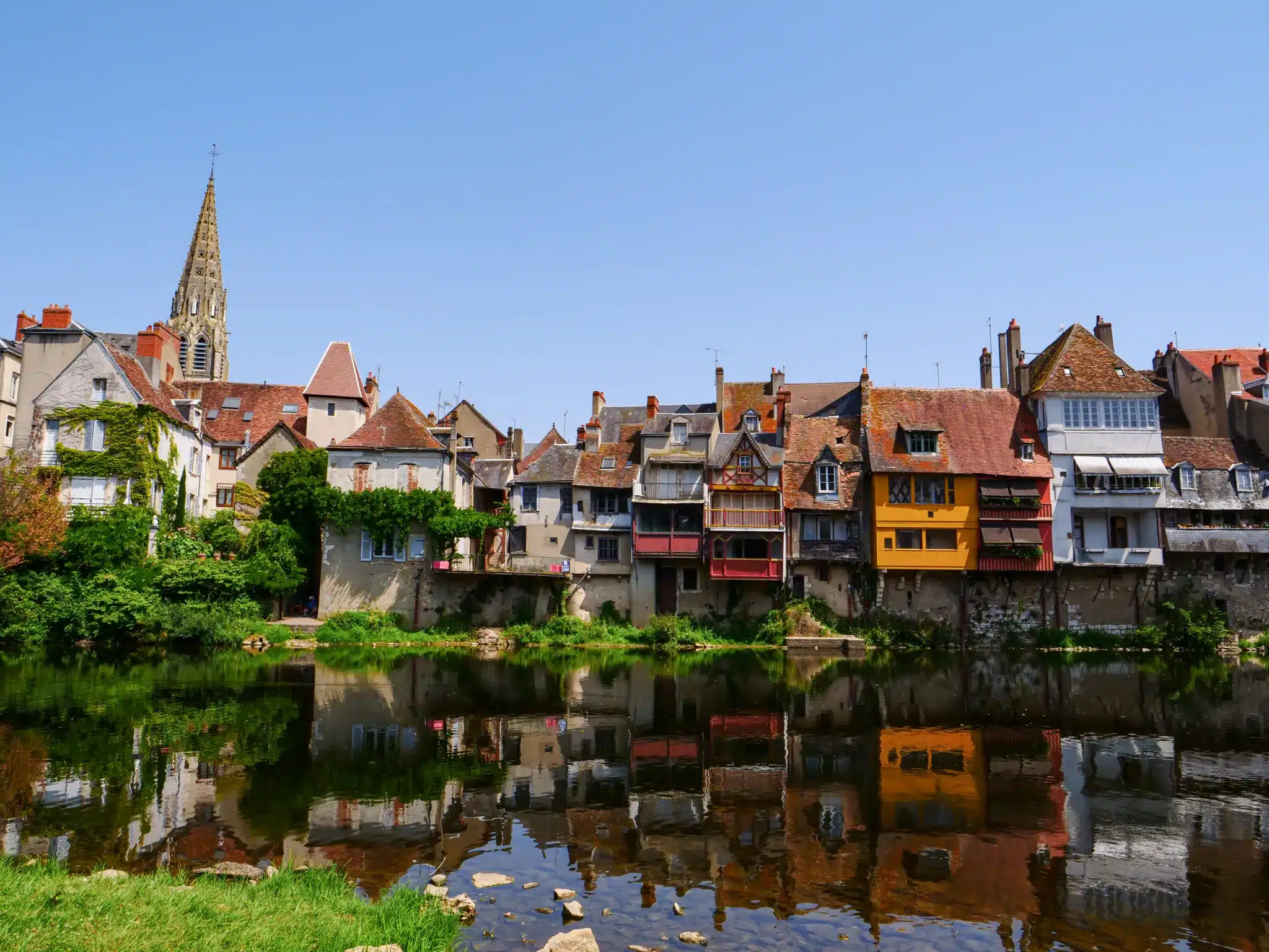 Vue d’Argenton-sur-Creuse dans l’Indre, avec ses maisons colorées au bord de la Creuse, leurs reflets dans l’eau et le clocher dominant la ville.