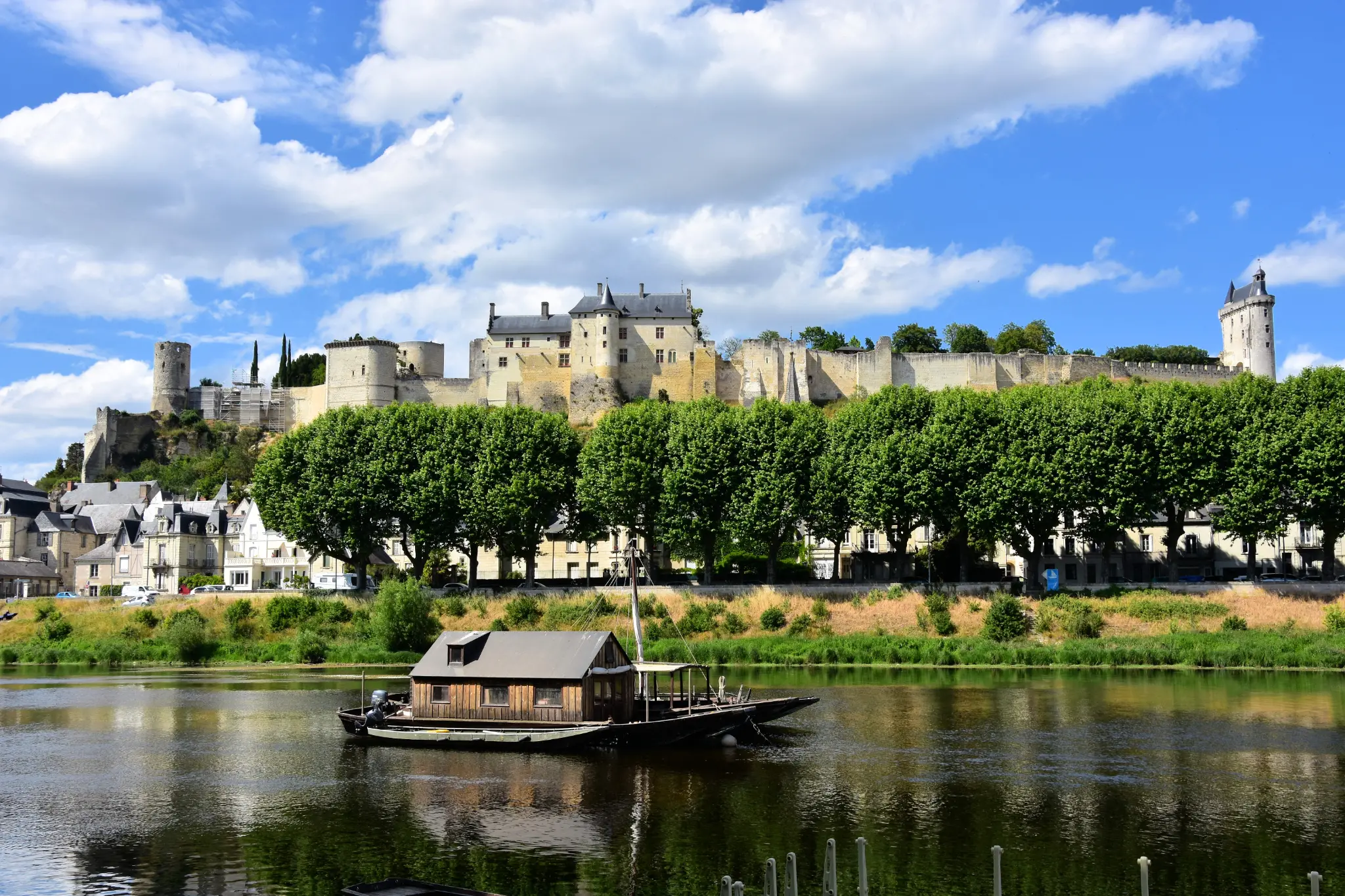 Vue de Chinon avec la Forteresse royale dominant la Vienne et un bateau traditionnel au premier plan.