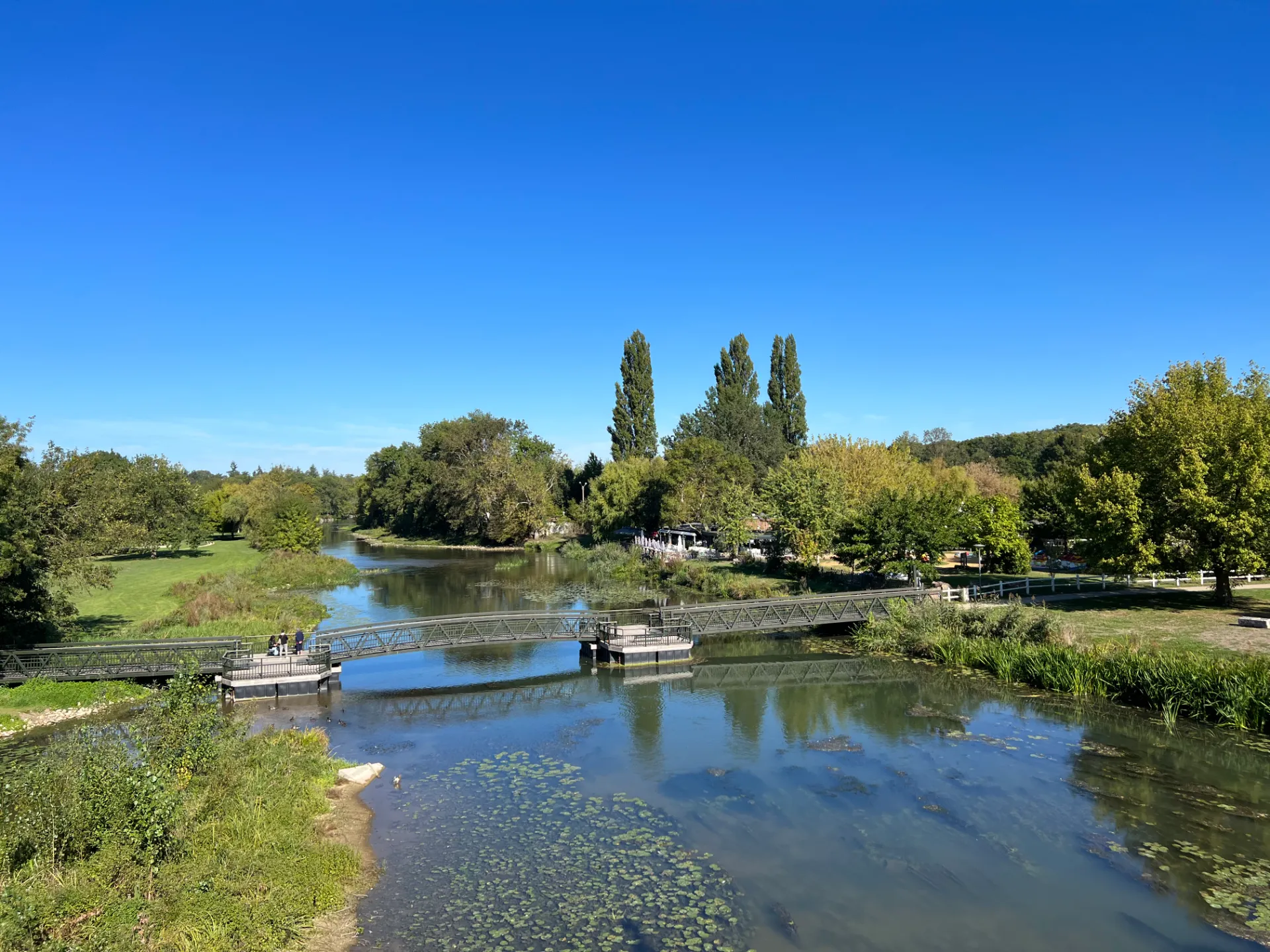 Vue sur l’Indre à Montbazon en Indre-et-Loire, avec la passerelle piétonne et les berges verdoyantes du parc de la Grange Rouge.