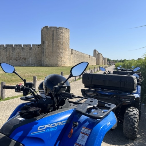 Balade en quad avec Camargue Loisirs Aventures à Aigues-Mortes, face aux remparts médiévaux sous un ciel bleu éclatant.