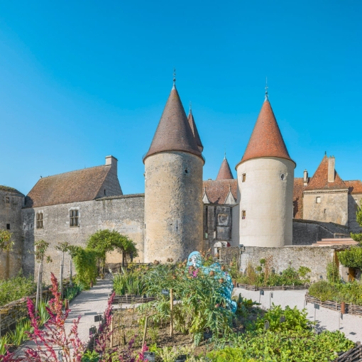 Château de Châteauneuf en Côte-d’Or avec ses tours médiévales et ses jardins fleuris sous un ciel bleu