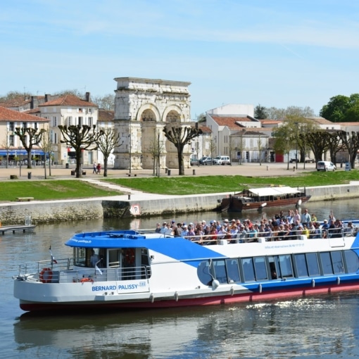Bateau de croisière fluviale naviguant sur la Charente à Saintes avec vue sur l’arc antique et les quais verdoyants