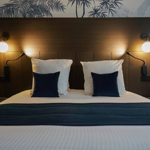 Lit double soigneusement préparé avec coussins bleus et éclairage tamisé dans une chambre d’hôtel à la décoration moderne.