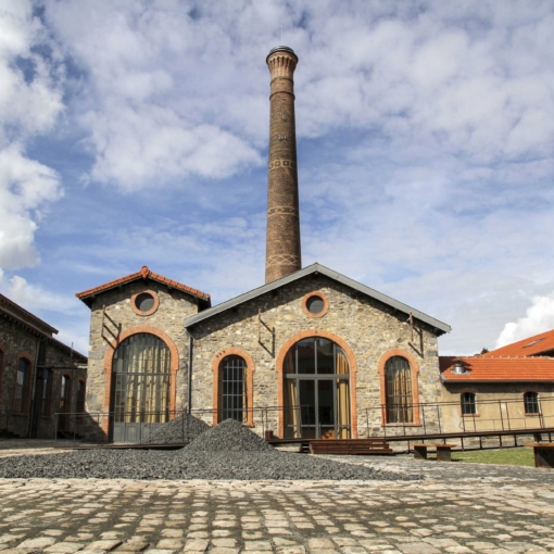 Façade en pierre et cheminée industrielle de l’Atelier-Musée du Chapeau à Chazelles-sur-Lyon, lieu emblématique retraçant l’histoire du savoir-faire chapelier en Auvergne-Rhône-Alpes.
