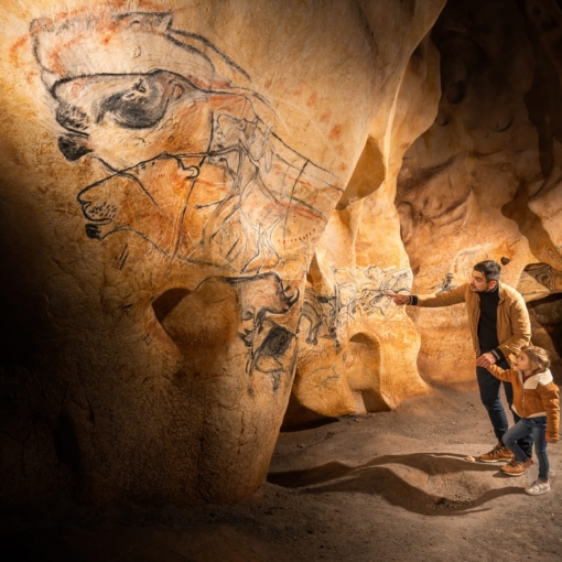 Un père et sa fille admirent les peintures préhistoriques reproduites dans la Grotte Chauvet 2 à Vallon-Pont-d’Arc.