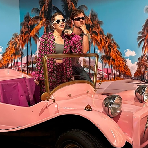 Visiteurs posant devant une voiture ancienne rose au Musée 1900, lieu insolite dédié aux objets et à l’ambiance rétro du siècle dernier