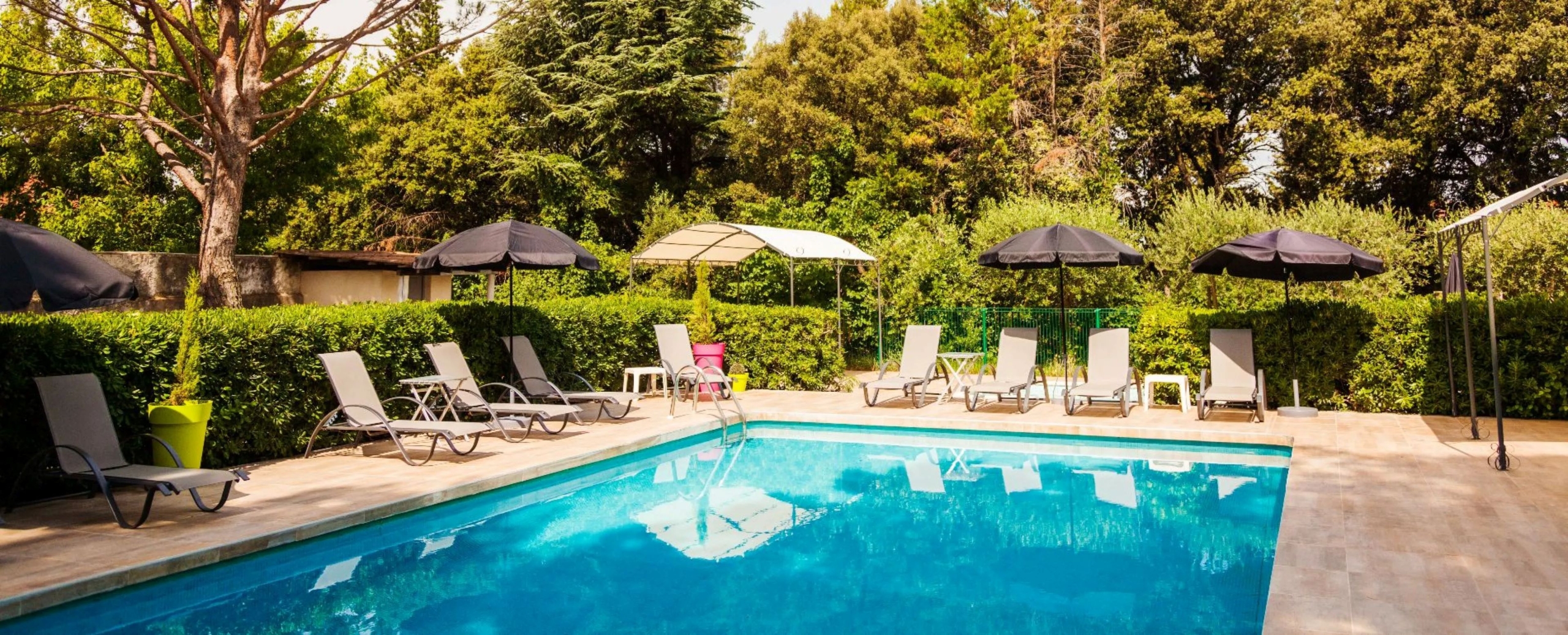 Piscine extérieure du Petit Manoir entourée d'un jardin arboré et d'espaces de détente en Provence.